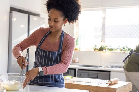 African american woman whisking batter in striped apron in sunlit modern kitchen
