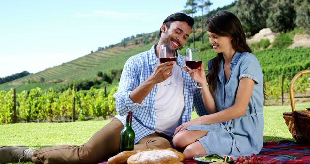 A couple is enjoying a romantic picnic with wine in a lush vineyard under a clear sky. This image is ideal for travel advertisements, romantic getaway promotions, wine tours, and lifestyle blogs focusing on outdoor leisure activities.