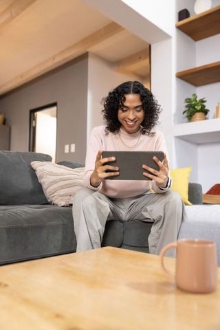 Smiling non-binary person holding tablet at home, cozy living room, remote work lifestyle