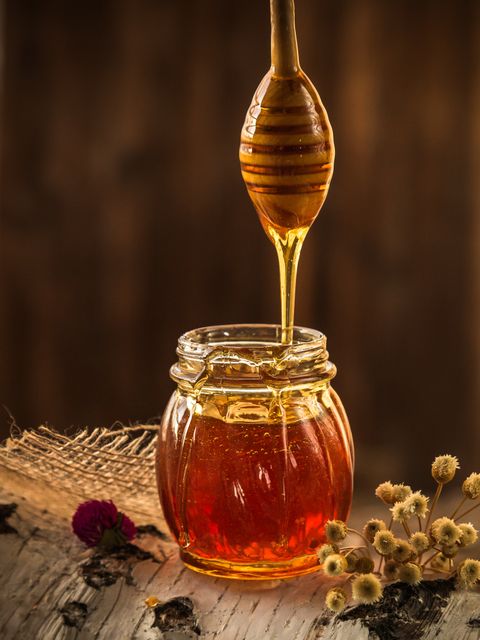 Photo capturing golden honey flowing from a wooden dipper into a glass jar. This image showcases the rich, natural sweetness of honey and the simple elegance of its presentation. Ideal for use in food blogs, natural product advertisements, cookbook illustrations, and health and wellness promotional materials.