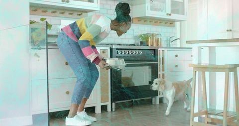 Bending woman offering metal dog bowl in bright farmhouse kitchen, cozy pet care moment