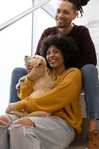 Smiling african american couple sitting on stairs holding golden retriever puppy, cozy moment