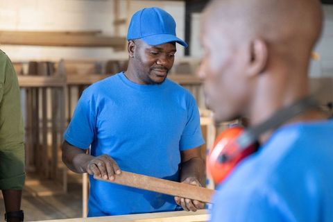 African american workers inspecting wooden plank in carpentry workshop showing teamwork