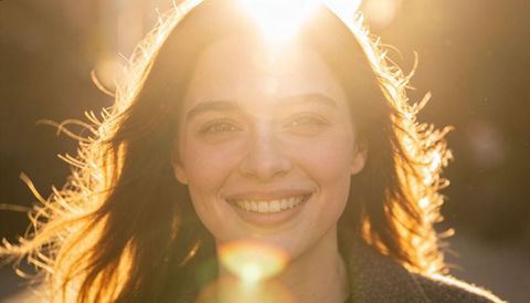 Young woman smiling in golden backlight with warm lens flare and glowing hair