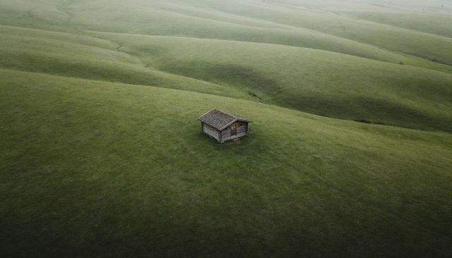 Weathered wooden cabin sitting on rolling green hills under misty overcast light