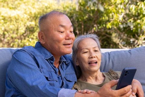 Senior asian couple sharing smartphone on garden sofa enjoying sunny outdoor moments