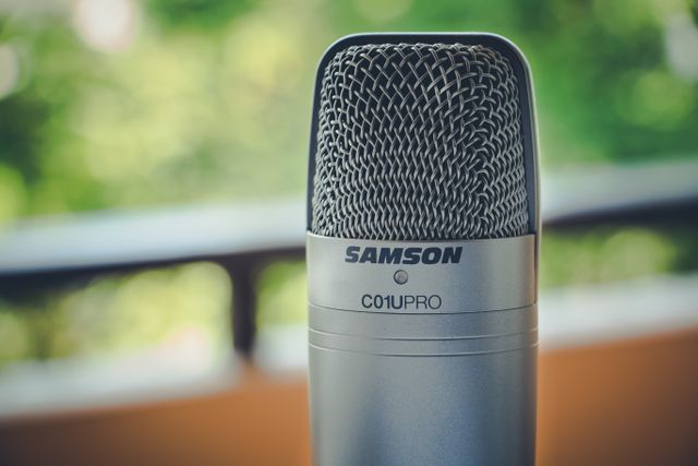Closeup view of a professional microphone with an outdoor background. This image is perfect for content related to audio recording, podcasting, voice-over work, and broadcasting. Ideal for illustrating articles, blogs, and media about studio equipment, sound technology, and professional audio setups.