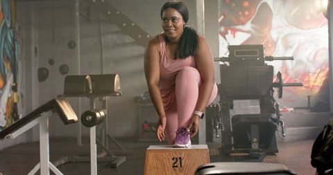 African american woman tying shoe on plyo box in urban gym, preparing for strength workout