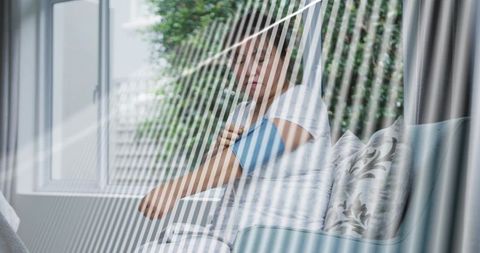 Senior man checking blood pressure on living room sofa with blue cuff and natural light