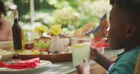 Happy afrian american boy holding drink at family dinner table in sunny garden, copy space - Download Free Stock Photos Pikwizard.com