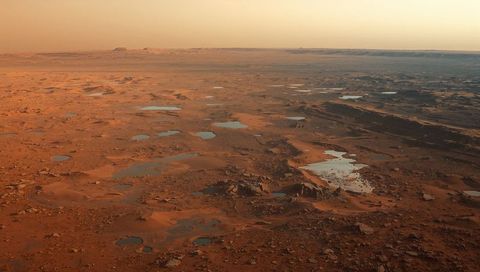 Rust-ochre rocky plain stretching to horizon, reflective shallow basins glowing at dusk