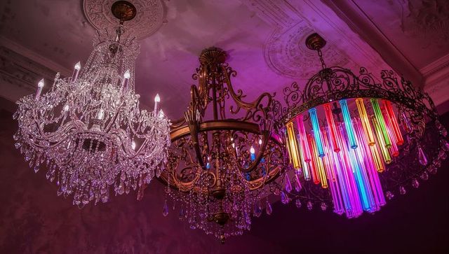 Opulent cut-crystal, brass and multicolor neon chandeliers hanging in baroque ballroom