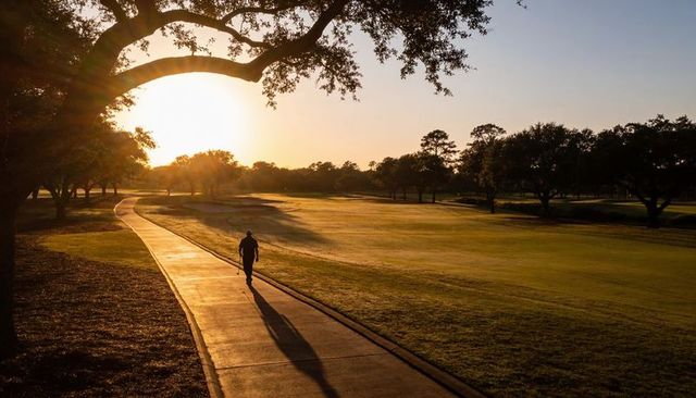 Walking man on sunlit golf cart path at golden hour under oak canopy