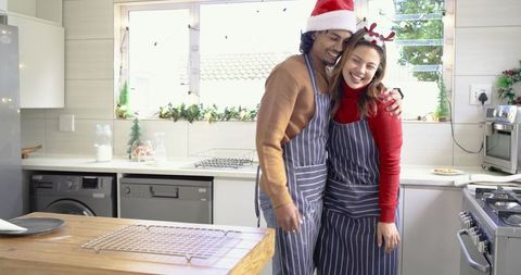 Couple hugging in festive kitchen wearing santa hat and reindeer antlers baking together