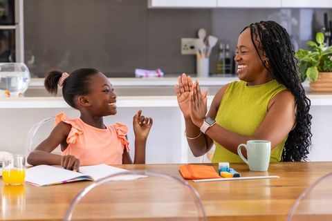 African mother and daughter high-fiving while doing homework at bright kitchen table
