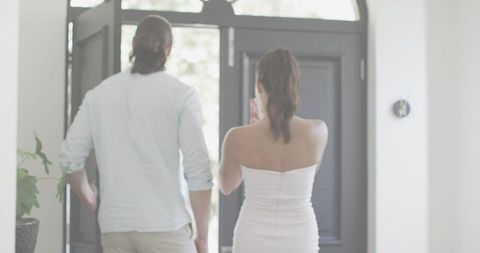 Couple entering modern home through bright foyer while woman checking smartphone at doorway