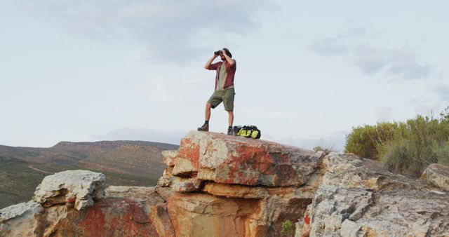 Caucasian male survivalist using binoculars, standing on mountain peak in wilderness - Download Free Stock Photos Pikwizard.com
