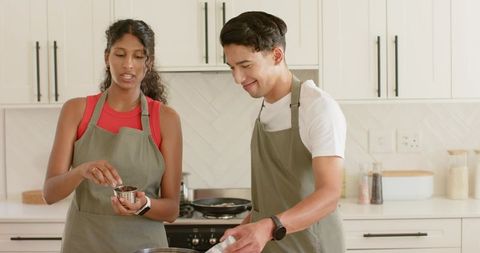 African american couple cooking together in modern white kitchen wearing olive aprons