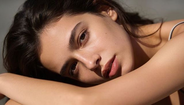 Young woman resting head on forearms in soft natural light closeup portrait for skincare