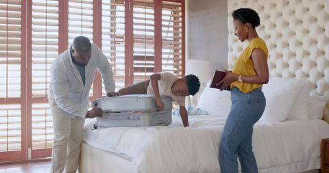 African American family packing suitcase together in sunlit bedroom preparing for trip