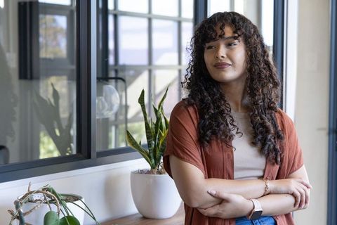 Young professional standing by window in modern coworking office with plants and calm vibe