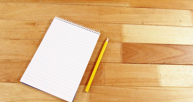A blank notepad with a yellow pencil on a wooden surface, with copy space. Ideal for educational or business concepts, the image conveys preparation for writing or note-taking.