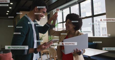 High-fiving Colleagues Celebrating Team Win in Modern Office Lounge with Laptop and Phone