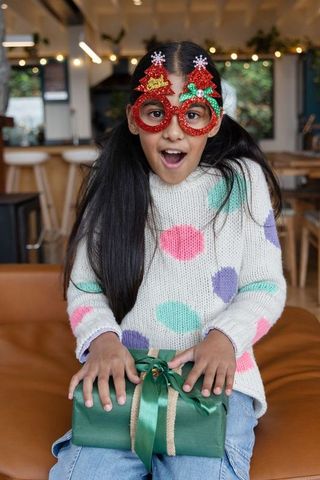 Surprised asian girl wearing glittery christmas tree glasses holding green wrapped gift