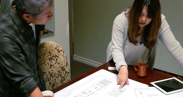 Two architects are focused on reviewing building plans in an office environment. They appear to be engaged in a discussion about the project details. This image is perfect for illustrating concepts related to teamwork, collaboration, professional planning, architectural projects, and interior design.