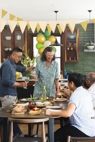 Multigenerational family celebrating at kitchen table with wine, balloons and bunting decor
