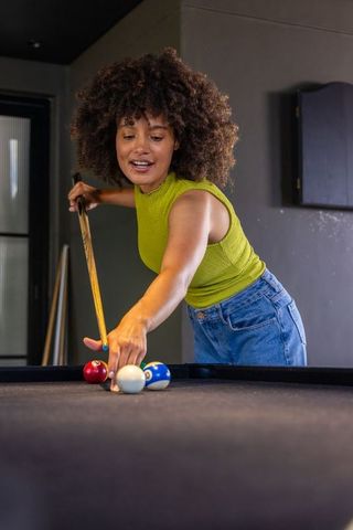 African american woman aiming cue on black-felt pool table in casual lounge recreation