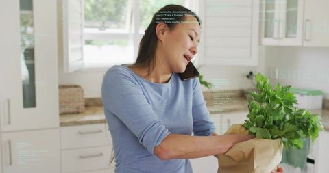 Woman multitasking on phone unpacking groceries in bright modern kitchen