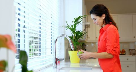 Caucasian Woman Washing Apple in Bright Kitchen
