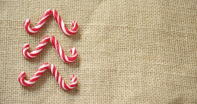 Red and white striped candy canes are arranged in a zigzag pattern on a burlap fabric background, with copy space. Candy canes often symbolize the festive spirit of Christmas and are popular as decorations and sweet treats during the holiday season.