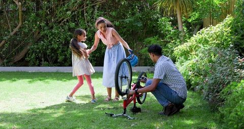 Father Repairing Bicycle with Daughters in Sunny Backyard