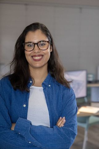 Confident professional woman smiling with tortoiseshell glasses standing in modern office