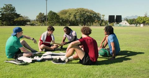 Youth cricket team sitting in huddle on grass field discussing strategy and teamwork