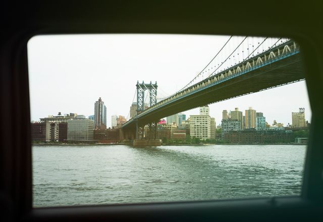 Manhattan Bridge framed by car window, overlooking urban skyline and river in New York City. Useful for themes of travel, urban architecture, city lifestyle, commuting, cityscapes, exploring metropolis.