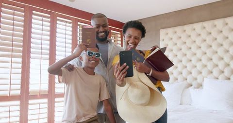 African american family posing selfie in hotel room with passports, straw hat, sunglasses