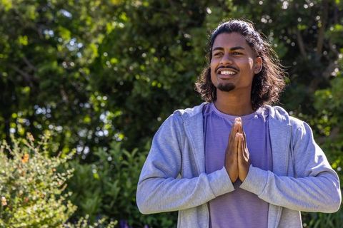 Young man practicing gratitude in sunlit garden wearing hoodie and purple top expressing mindfulness