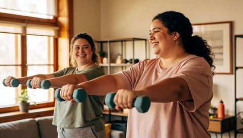 Smiling women exercising with teal dumbbells in sunlit cozy living room