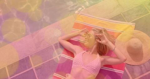 Young woman sunbathing on pool deck wearing pink polka-dot bikini and straw hat
