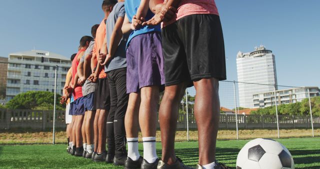 Diverse male football players standing with hands behind back on outdoor pitch. Football, sports and teamwork.