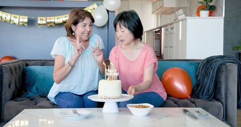 Senior Women Celebrating Birthday blowing cake at Home Party