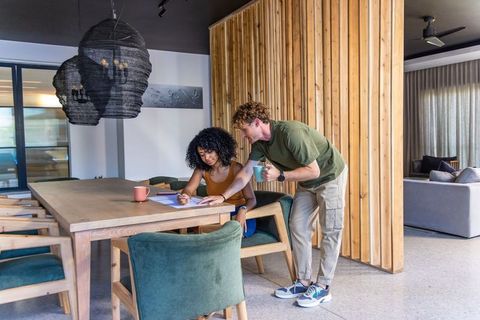African american woman and man reviewing documents with mugs at modern wood dining table