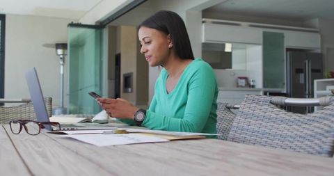 Woman at Laptop on Outdoor Patio Using Smartphone Near Home Kitchen
