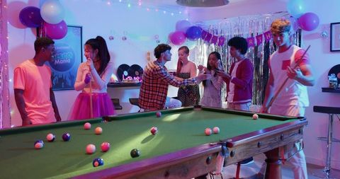 Friends toasting and playing pool at colorful birthday party in home game room