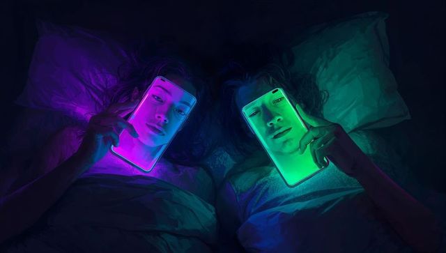 Couple lying in bed at night illuminated by smartphones