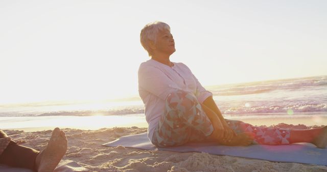Senior woman practicing yoga on beach at sunrise. Ideal for promoting mindfulness, wellness programs, senior fitness, healthy living, advertisements related to fitness, wellbeing, and calming lifestyle products.