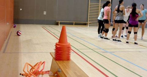 Diverse female volleyball team huddling during indoor practice with training cones